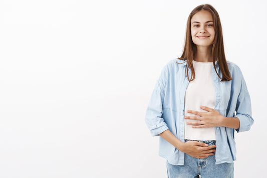 A smiling woman holding her stomach, looking healthy and happy. She has a glowing complexion and a confident expression, indicating her good gut health.